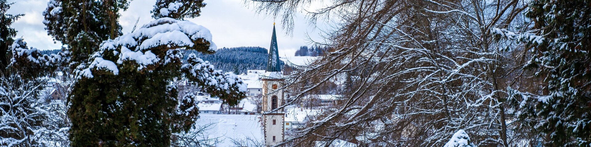 A snow-covered landscape with a church, trees, and houses.
