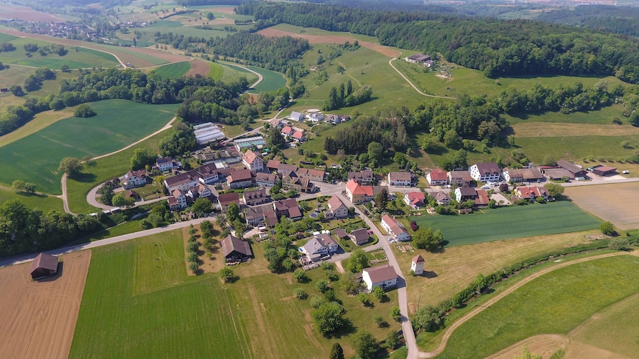 Vista aérea de un pueblo rural con casas, campos y un camino sinuoso.