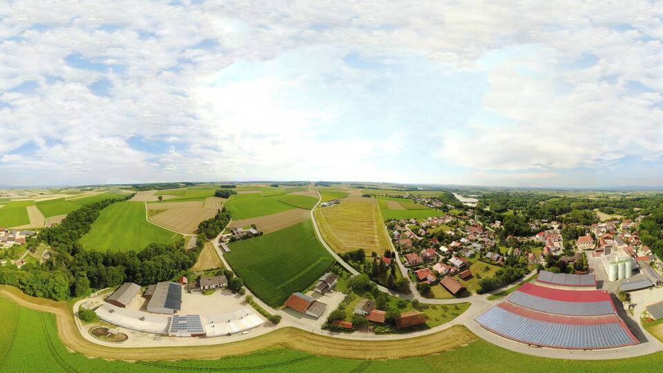 An aerial view of a rural landscape with fields, a small village, and solar panels.