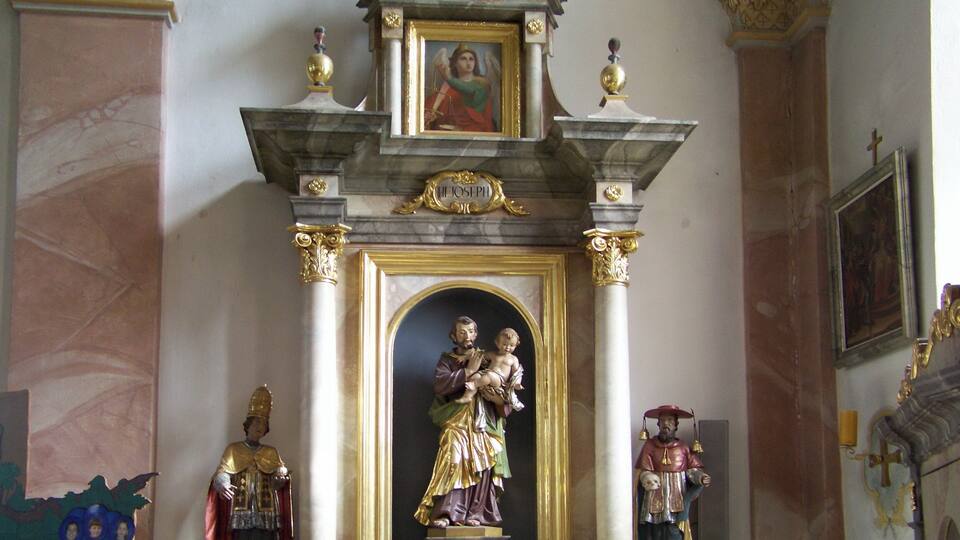 A religious altar with a statue of a saint, a framed painting, and a crucifix.