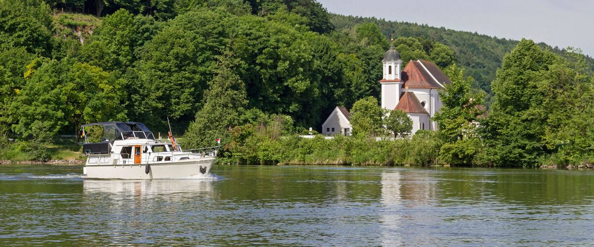 A boat on a calm river, surrounded by lush greenery and a church with a red roof.