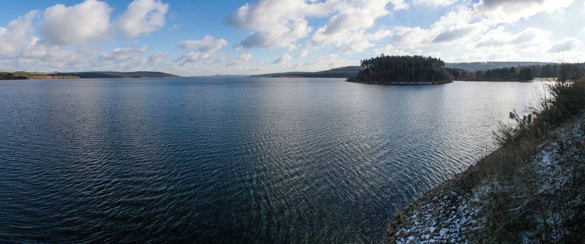 A calm lake with a small island in the center, surrounded by hills and a clear sky.