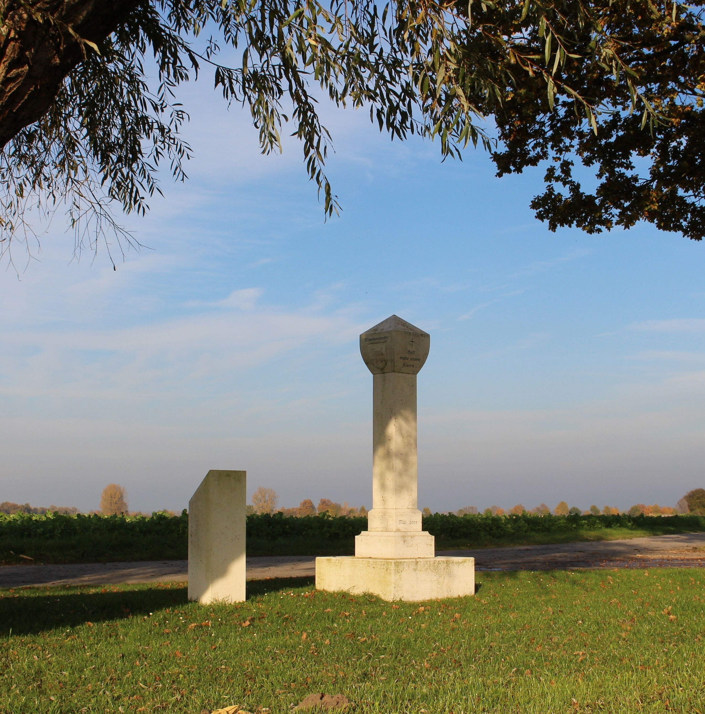 Two stone monuments in a grassy field with trees in the background.