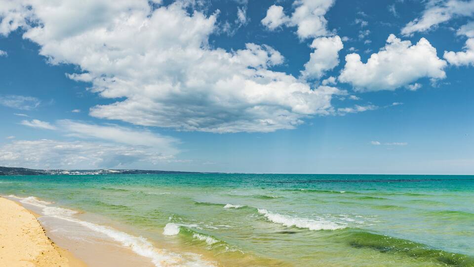A beach with clear turquoise water and a sandy shore under a partly cloudy sky.