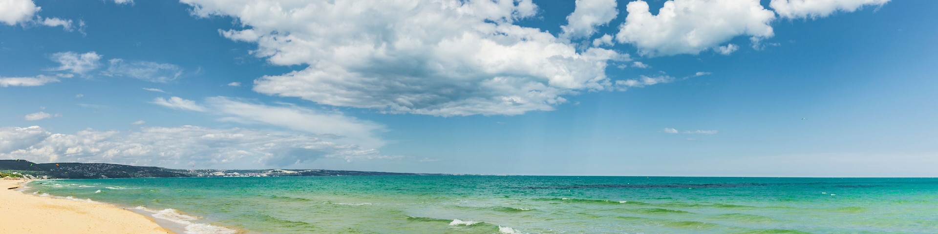 A beach with clear turquoise water and a sandy shore under a partly cloudy sky.