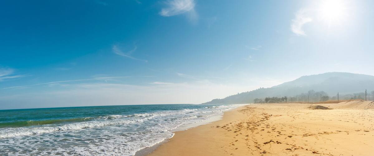 A beach with waves, a clear sky, and a mountain in the background.