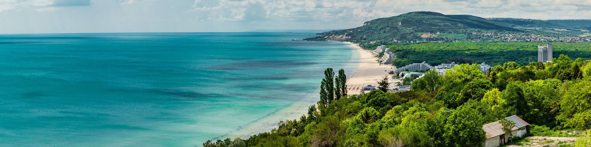 A coastal landscape with a beach, a mountain, and a town.