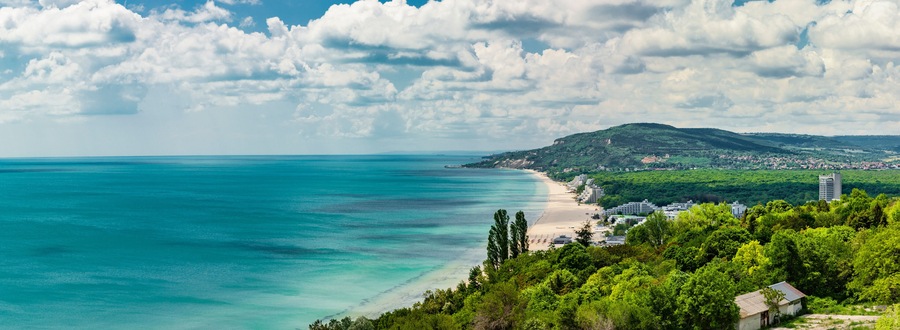 A coastal landscape with a beach, a mountain, and a town.