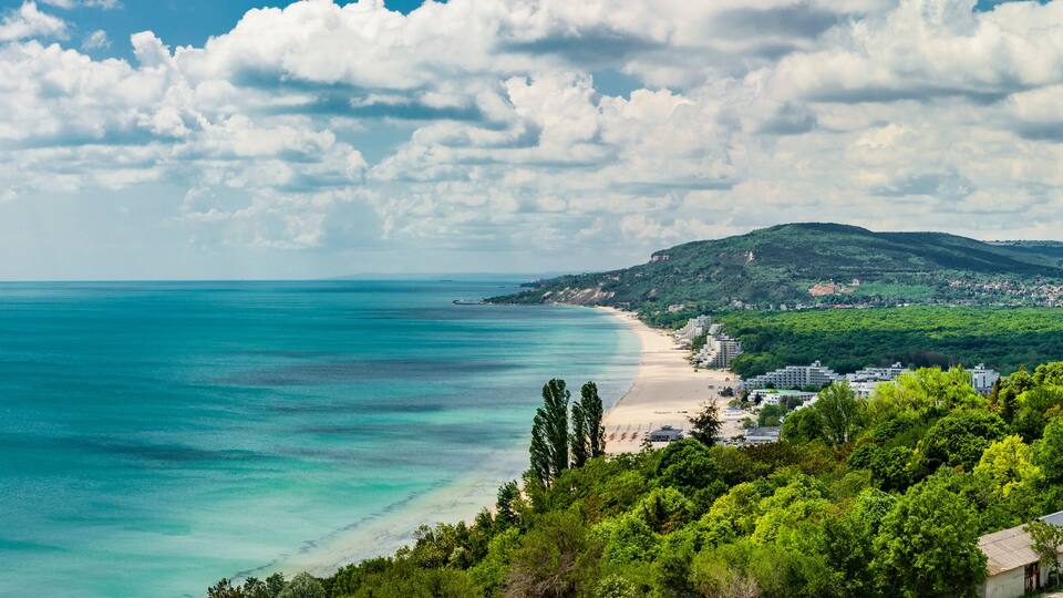A coastal landscape with a beach, a mountain, and a town.