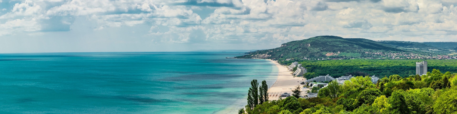 Un paisaje costero con una playa, una montaña y un pueblo.
