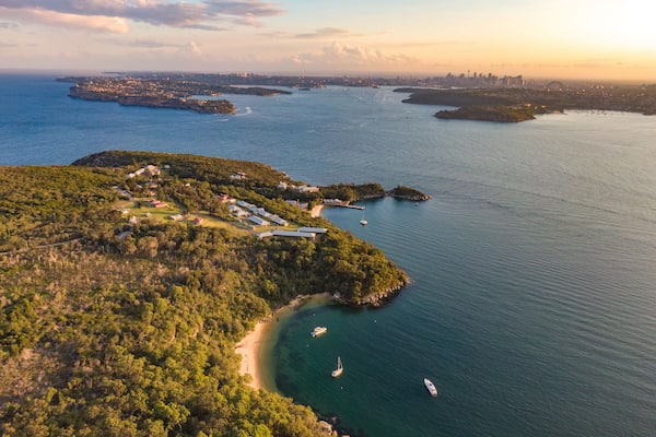 Aerial drone evening view of the Quarantine Station, part of Sydney Harbour National Park. Store Beach in foreground. Sydney harbour with North Head & South Head and city skyline in background.