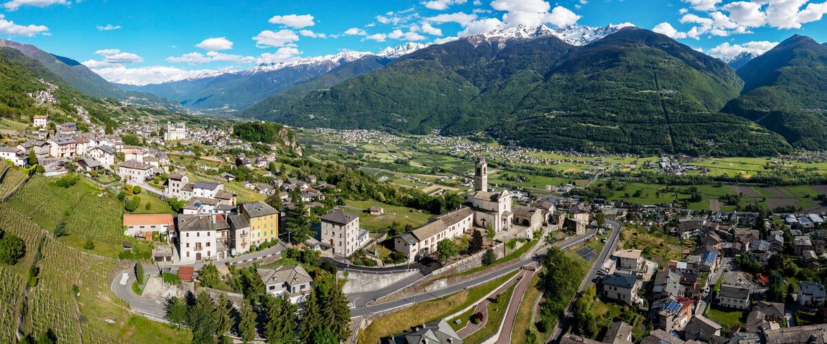 A mountainous landscape with a town nestled in a valley, surrounded by lush greenery and snow-capped peaks.