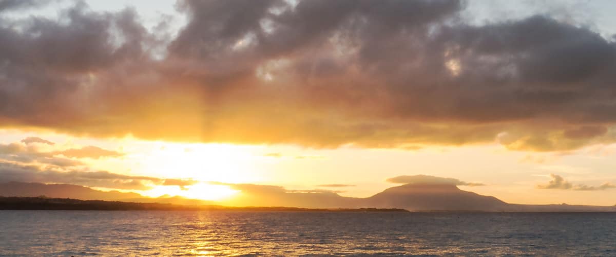 A sunset over a body of water with clouds and distant landforms.