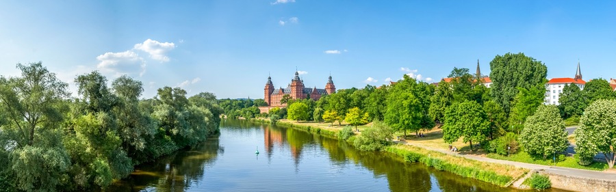 Ein Fluss mit einer Brücke, üppigem Grün und einem historischen Gebäude mit Türmen.