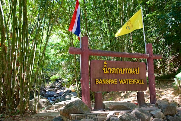 Ein Schild für den Bangpnae Wasserfall mit thailändischen Schriftzeichen und einer Flagge.