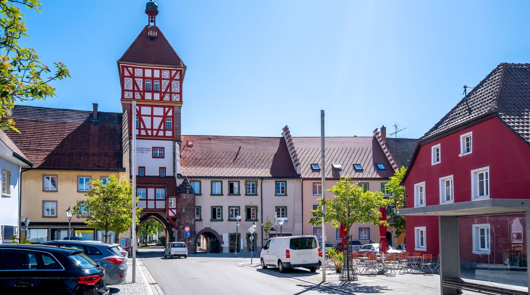 A town square with traditional European architecture, including a tower with a clock and a red building with white windows.