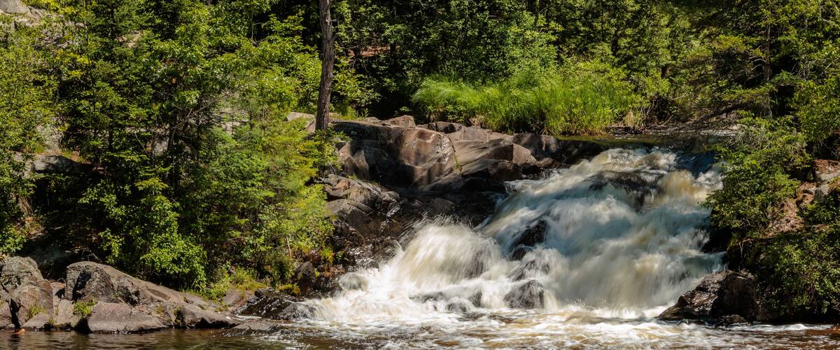 A waterfall in a forested area with rocks and greenery.
