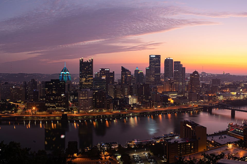 Une vue sur les gratte-ciel d’une ville au crépuscule, avec une rivière et un pont.