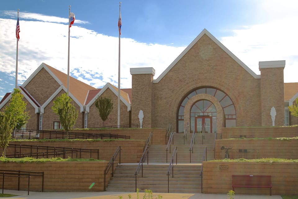 A large brick building with a triangular roof, multiple flagpoles, and a central entrance with steps.