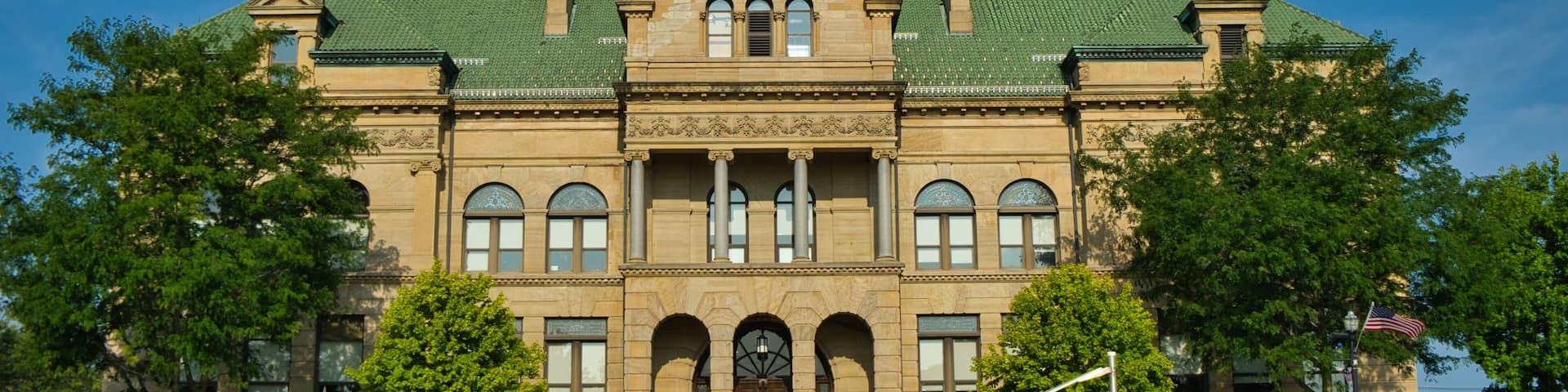 A large, historic building with a clock tower, arched windows, and a green roof.