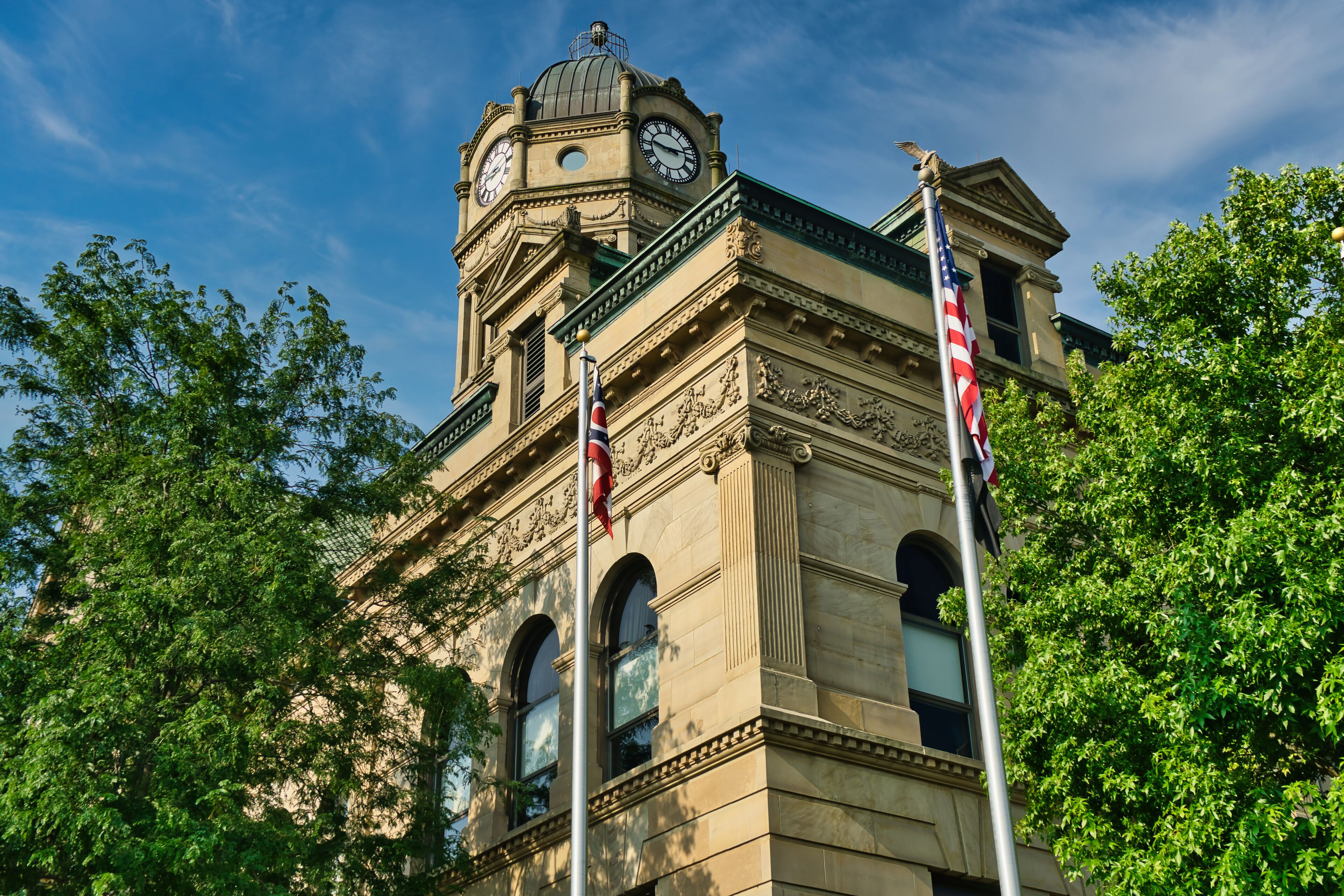 A historic building with a clock tower, ornate architecture, and American flags.