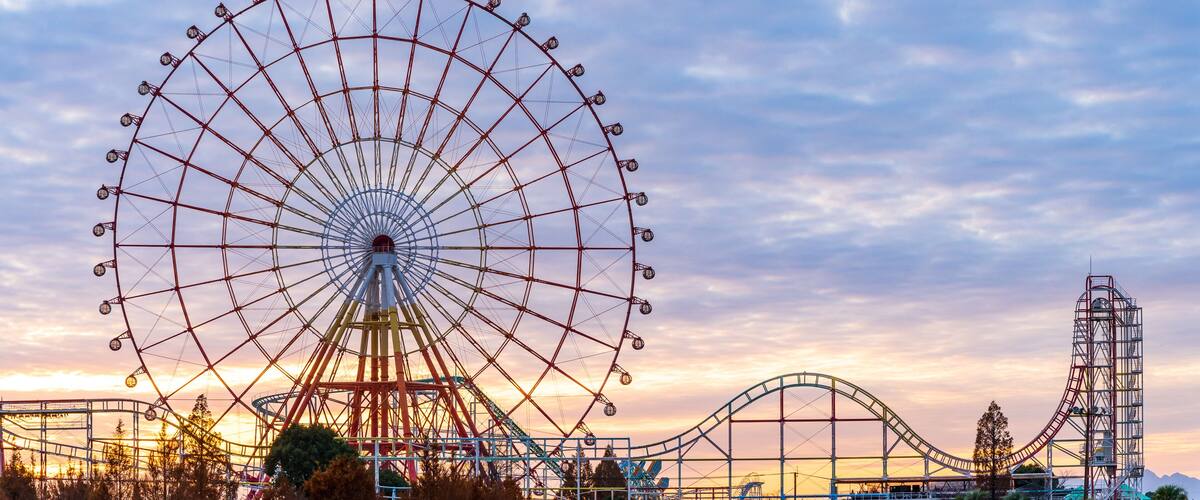 A large Ferris wheel and a roller coaster at an amusement park during sunset.