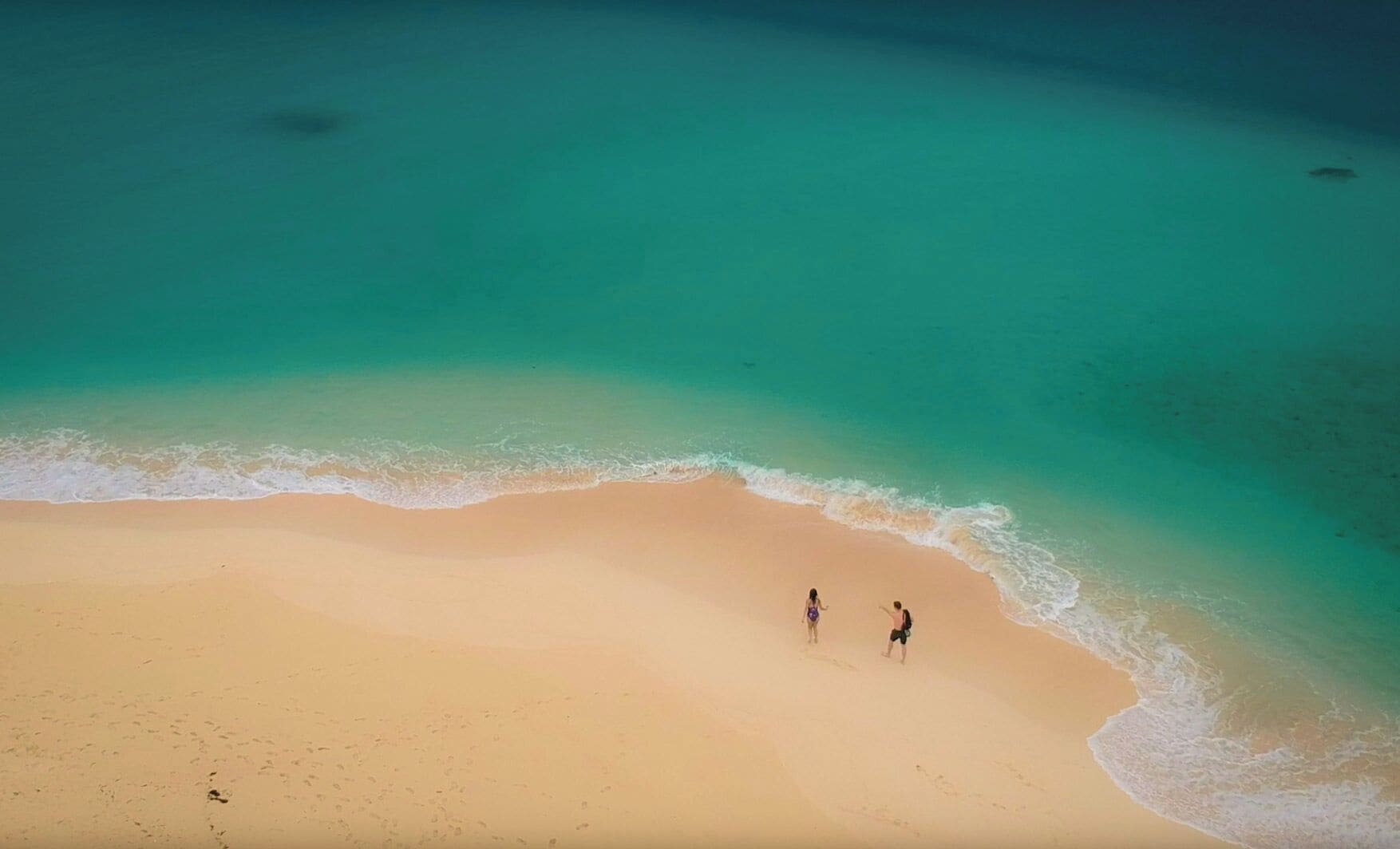 An aerial view of a beach with two people walking along the shoreline.