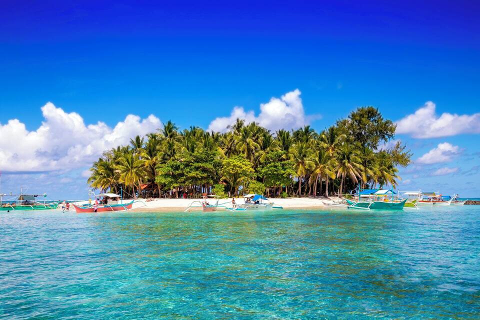 Una isla tropical con aguas turquesas cristalinas, palmeras y embarcaciones tradicionales.