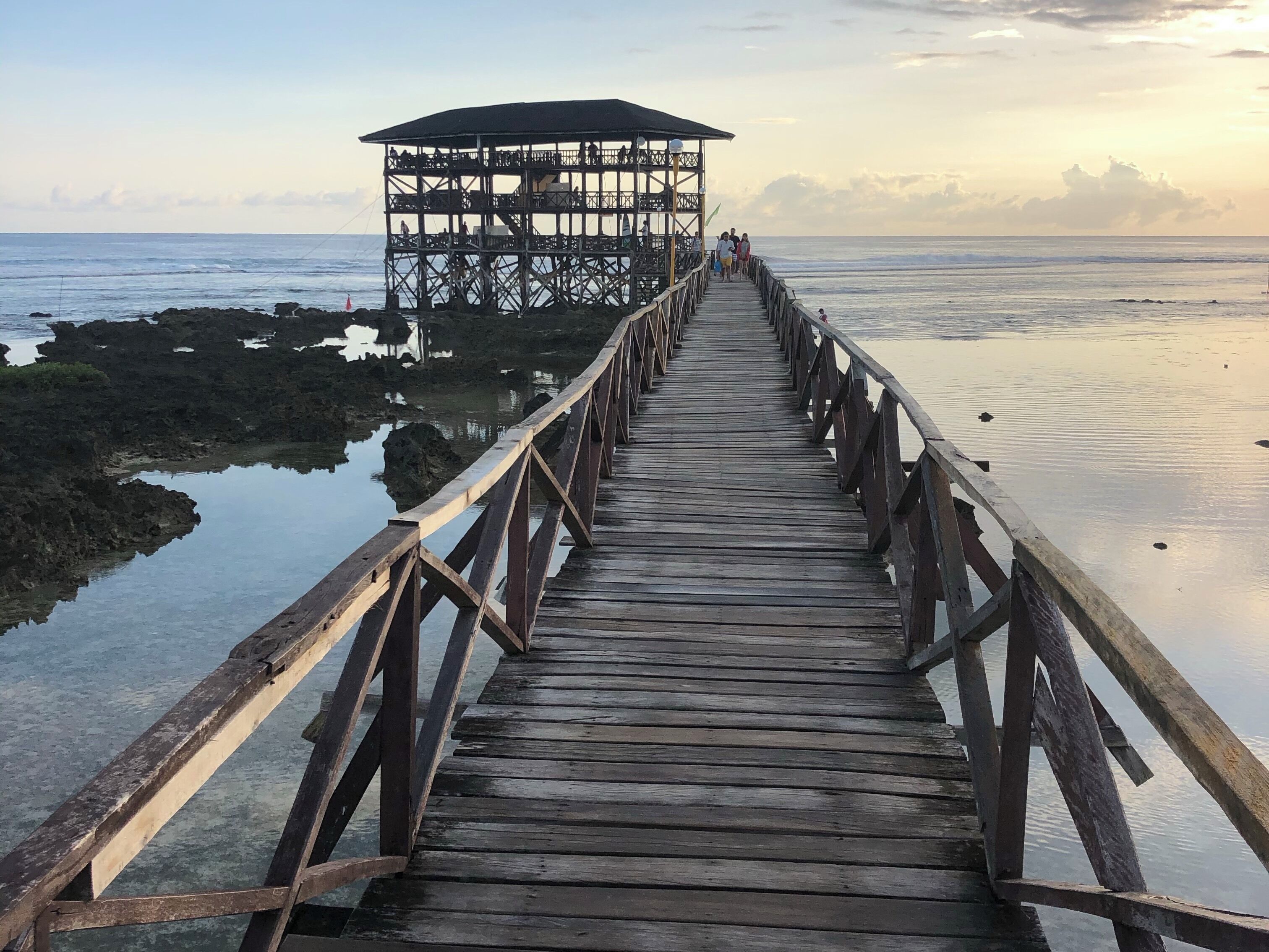 A wooden pier leading to a covered structure by the sea.