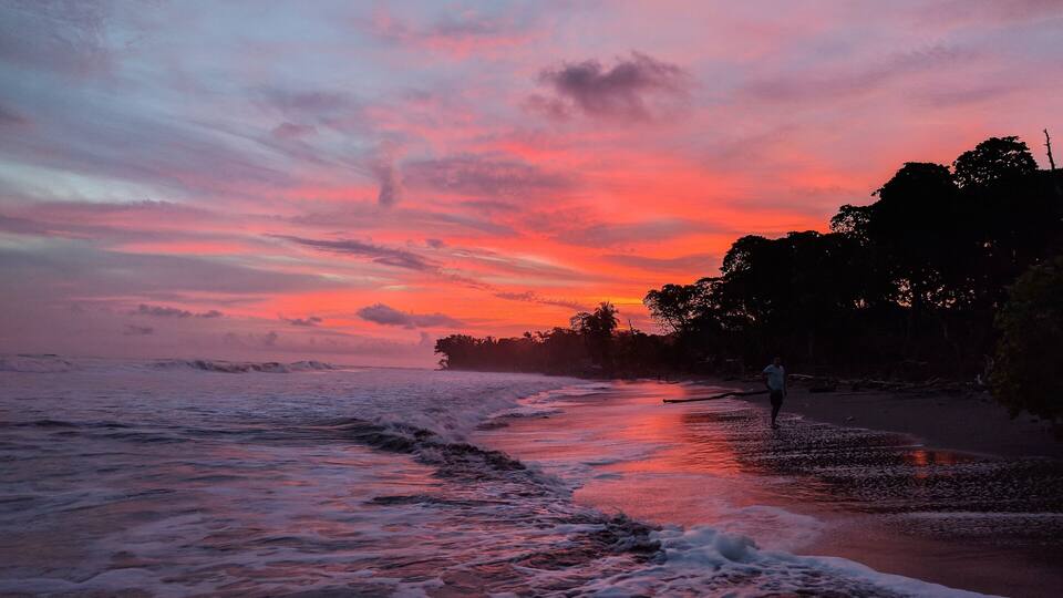 A beach at sunset with waves and a person walking.