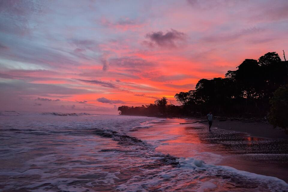 A beach at sunset with waves and a person walking.