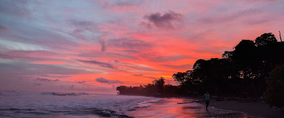A beach at sunset with waves and a person walking.