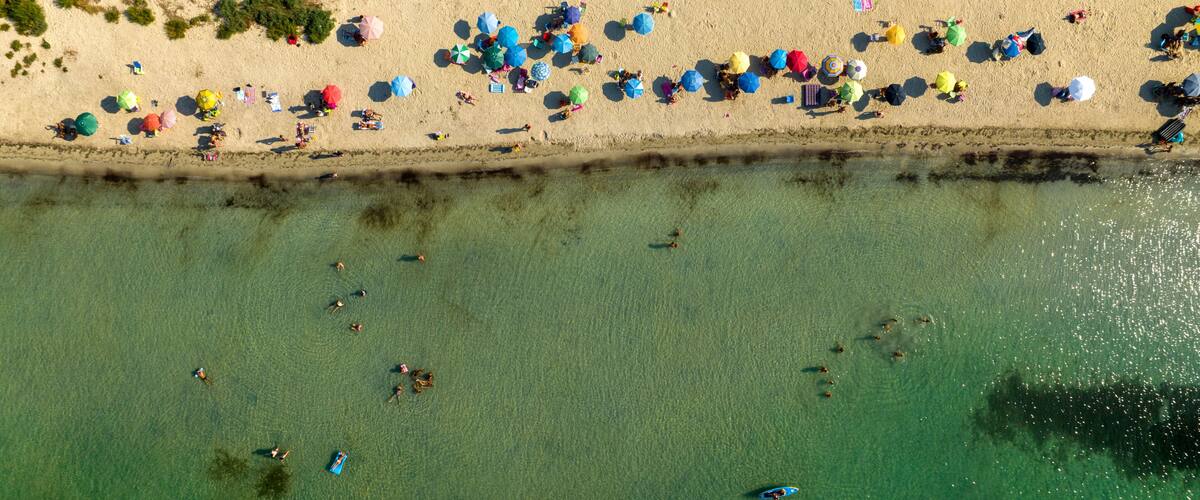 An aerial view of a beach with people, umbrellas, and boats.