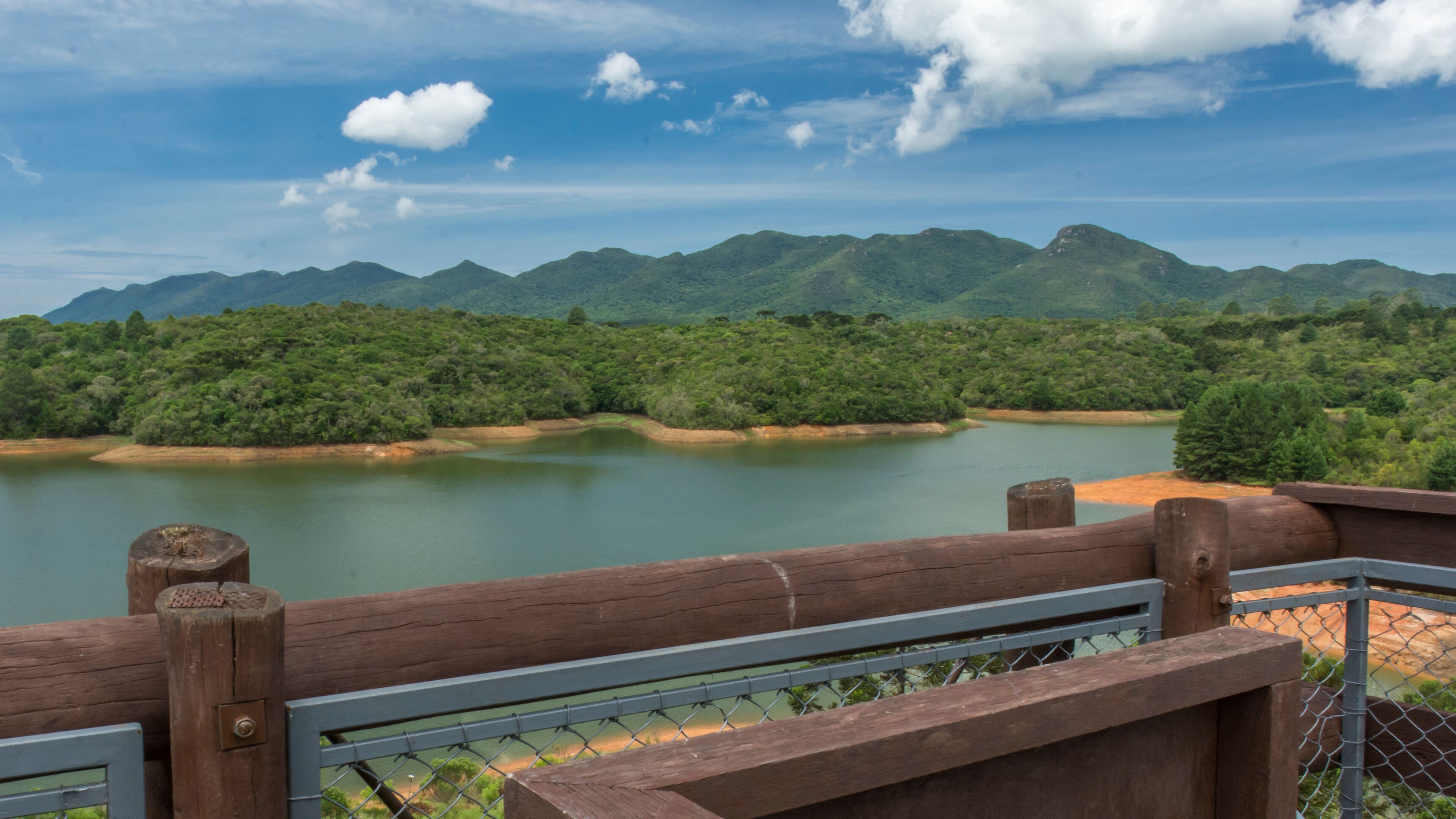 A river with mountains in the background and a wooden fence in the foreground.