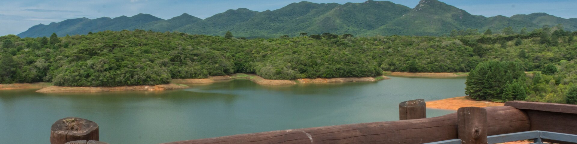 A river with mountains in the background and a wooden fence in the foreground.