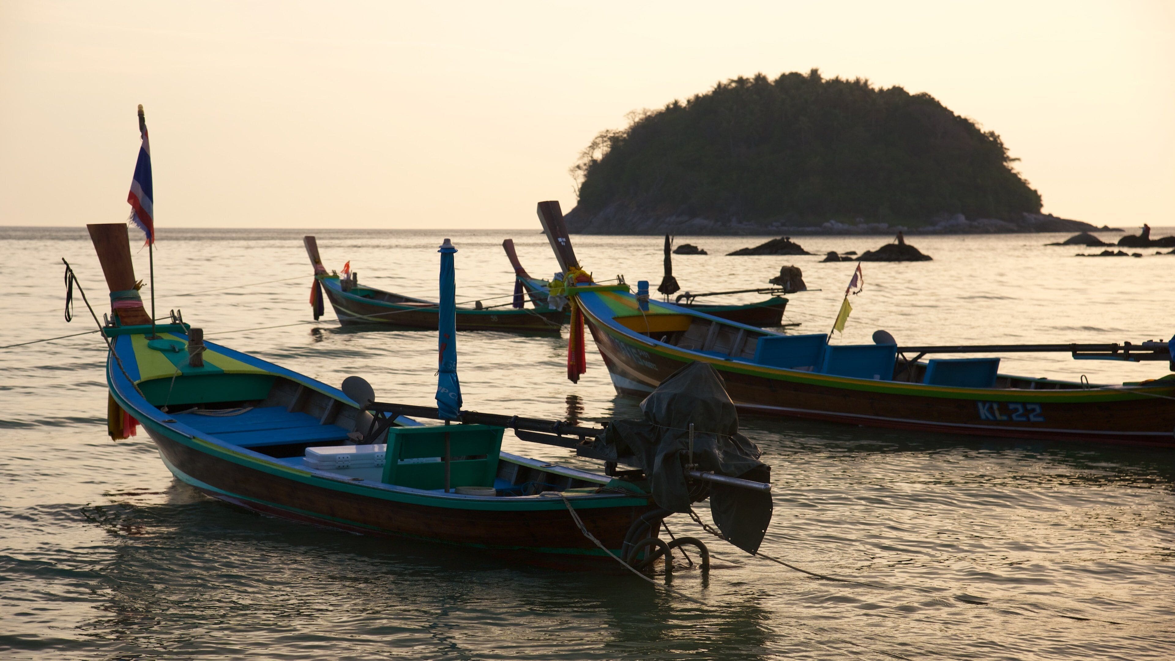 A row of colorful boats anchored near a small island at sunset.