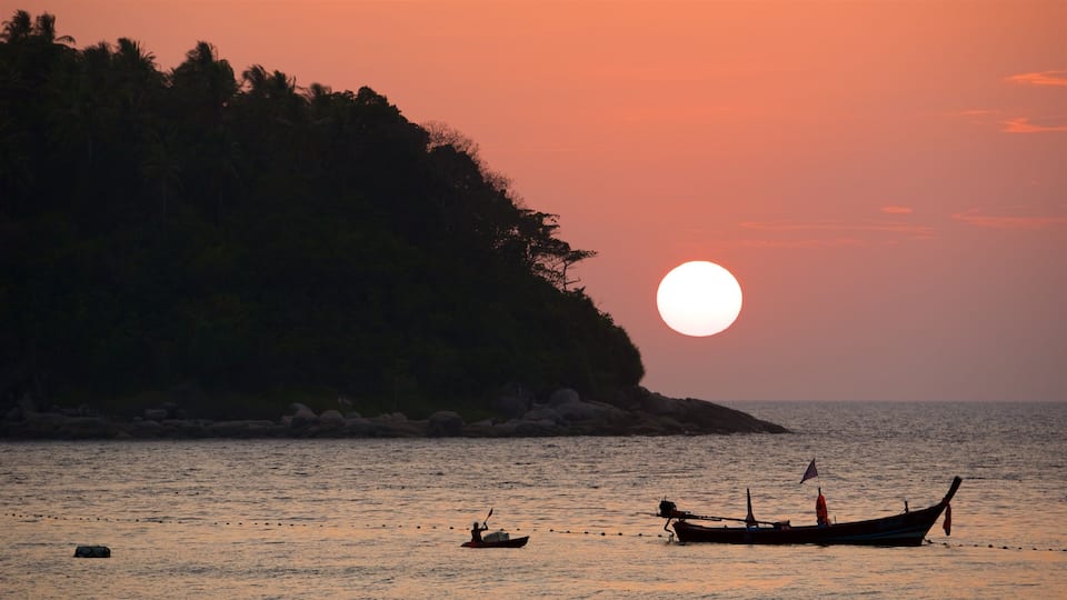 A sunset over a calm sea with a boat and a small island in the background.
