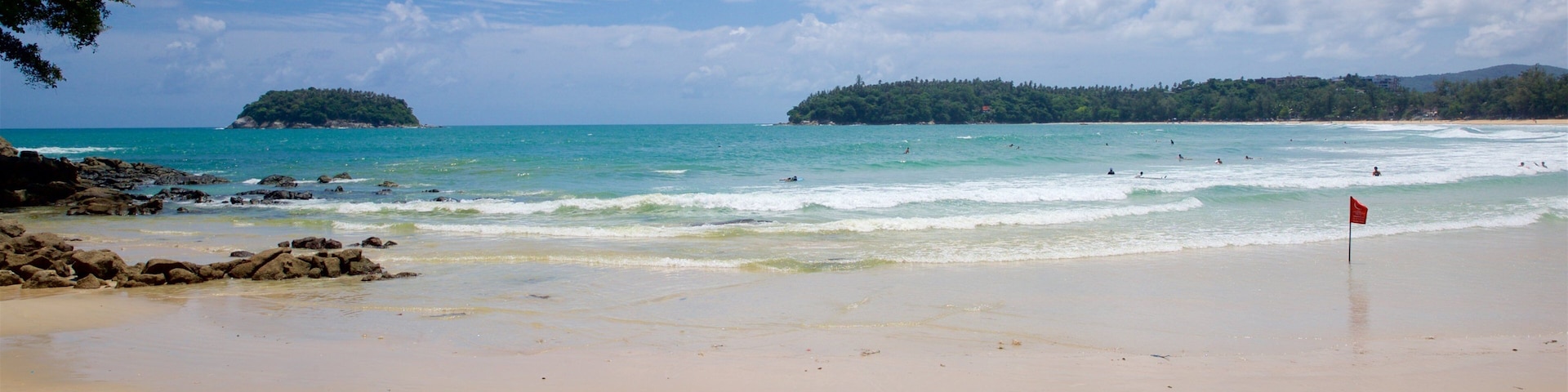 Una playa arenosa con aguas tranquilas, una bandera roja y una isla distante.