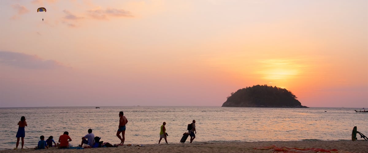 A beach at sunset with people relaxing and a kite flying.