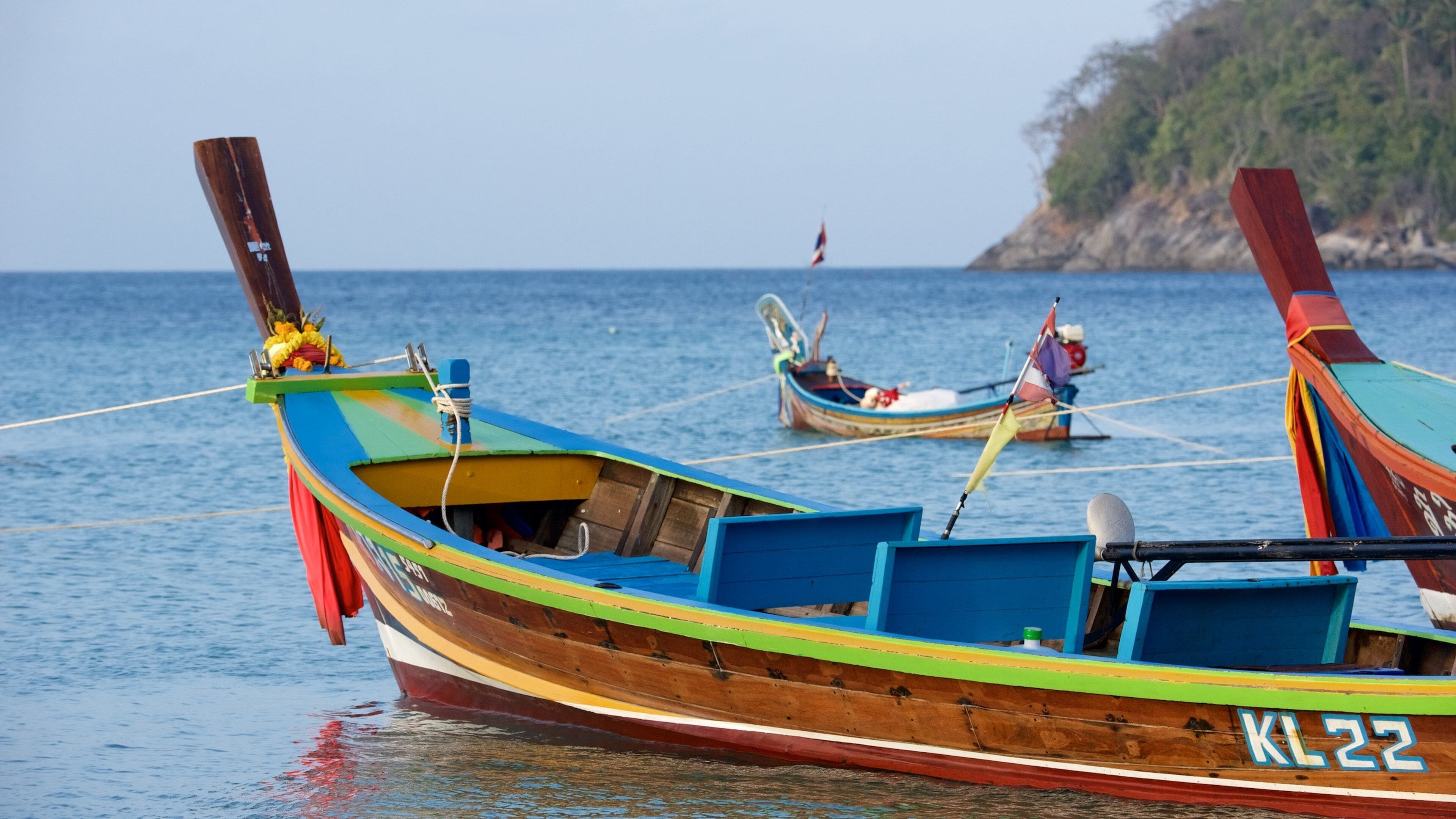 A colorful boat with the number KL22 on its side, anchored in calm waters with another boat in the background.