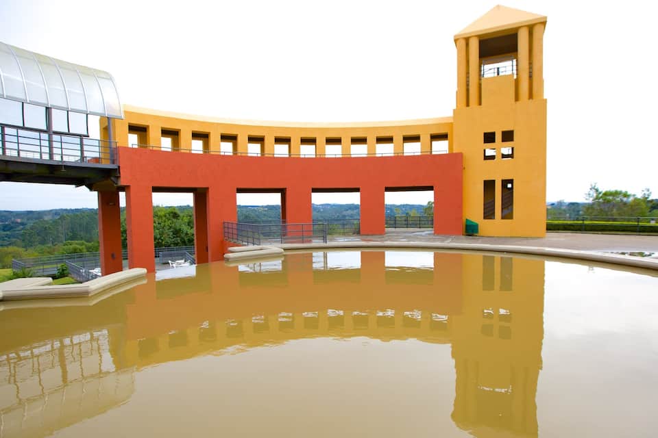 A modern architectural structure with a reflective pool, featuring a curved design and a tower.