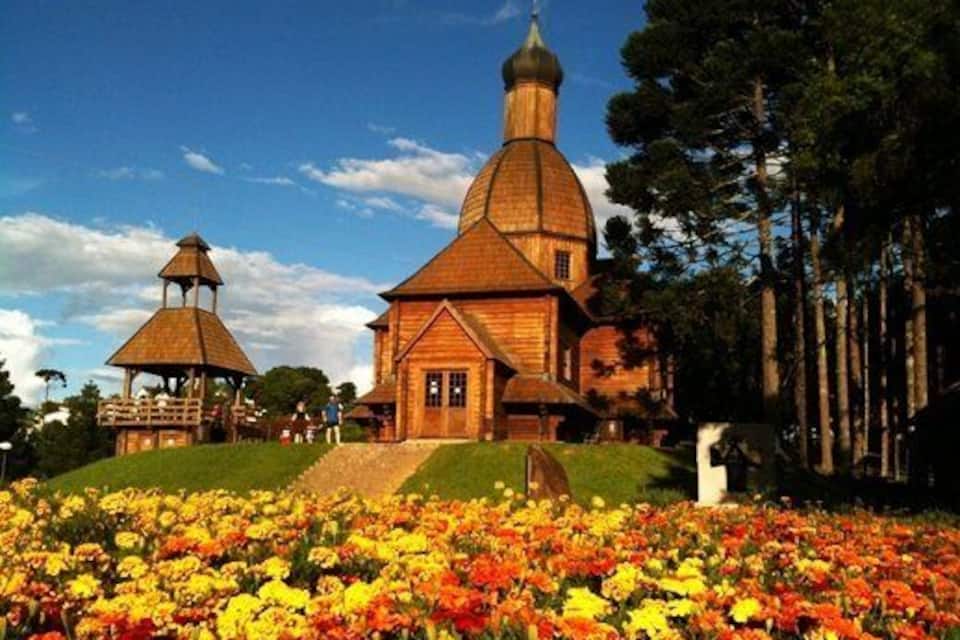 Eine Holzkirche mit einem Glockenturm und einem Pavillon, umgeben von bunten Blumen.