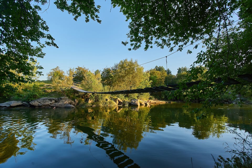 A calm river with reflections of trees and a wooden bridge.