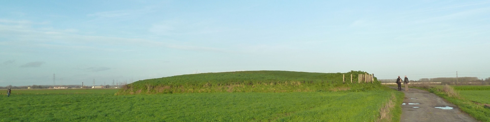 A green field with a dirt path and two people walking.