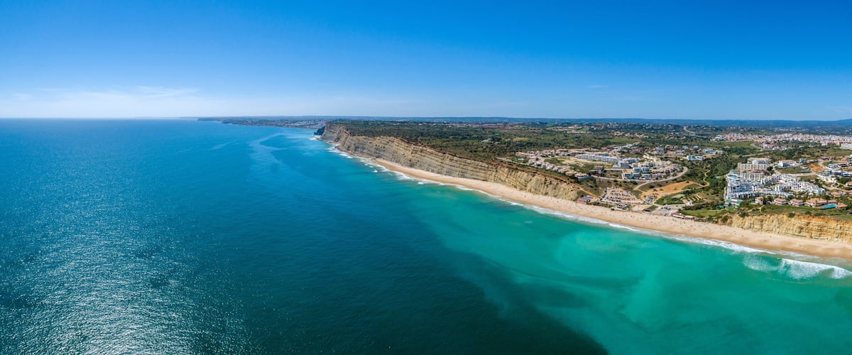 A coastal city with a long beach, clear blue waters, and a hilly landscape.