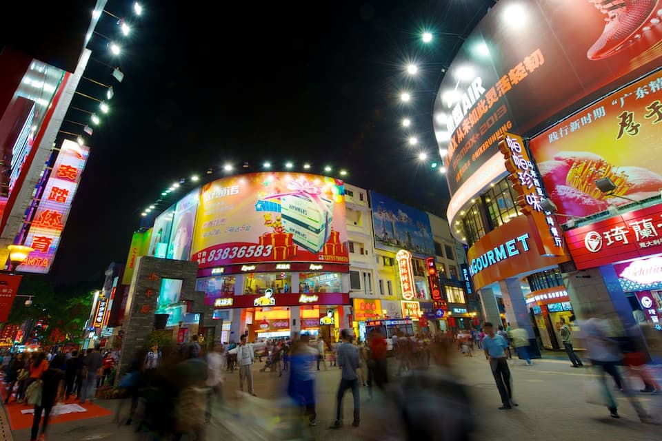Un pasaje comercial bien iluminado con letreros luminosos y una multitud de personas.