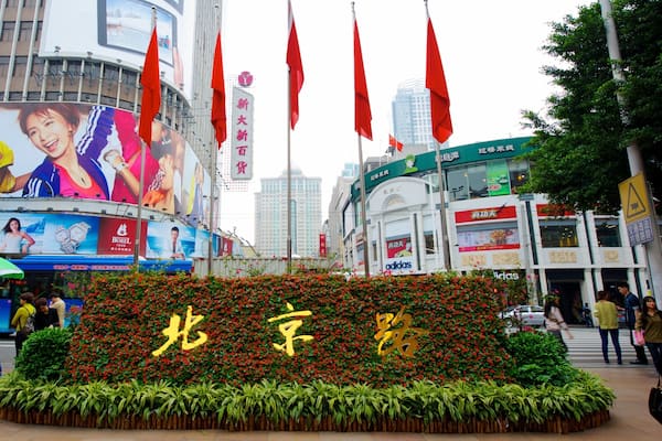 A large outdoor advertisement with red flags, a billboard with people, and a building with Chinese characters.