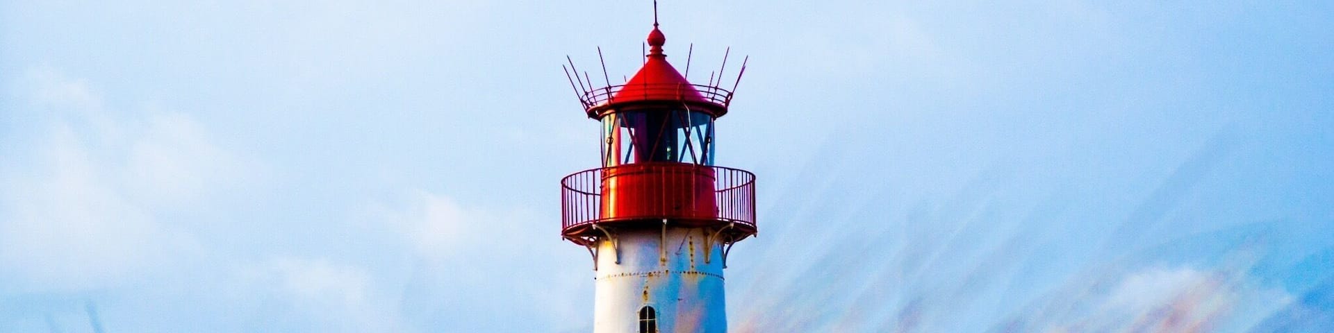 A lighthouse with a red top and white base, surrounded by tall grass.
