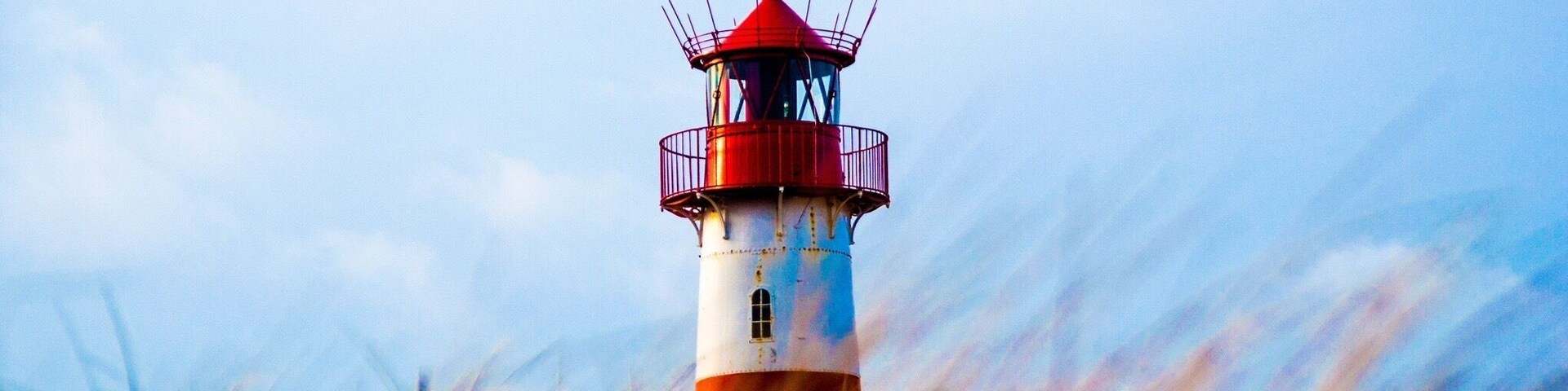 Um farol com a parte superior vermelha e a base branca, rodeado por grama alta.