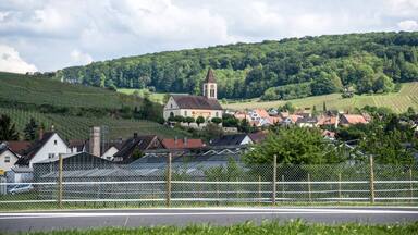 A village with a church, houses, vineyards, and a hill in the background.